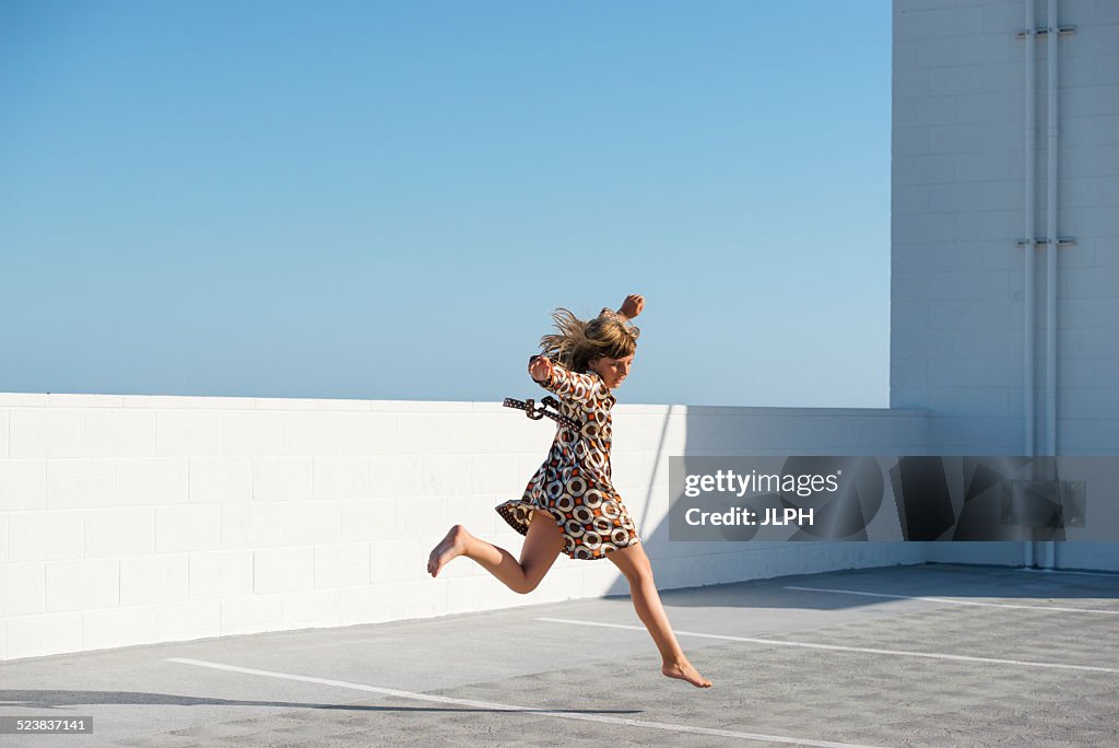 Girl jumping barefoot on building rooftop