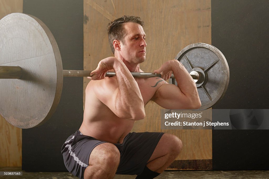 Mid adult male weightlifter lifting barbell in gym