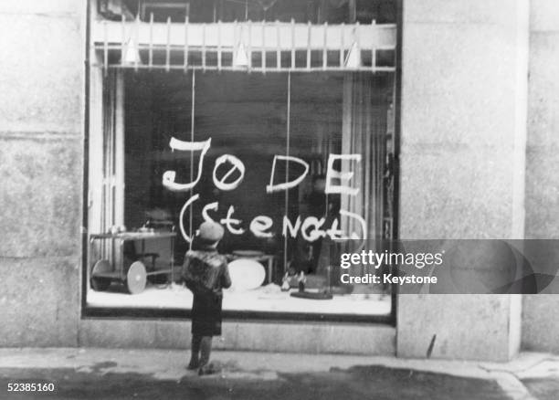 Anti-semitic graffiti on a shop window in Oslo, 1941. A small boy reads the message 'Jew '.