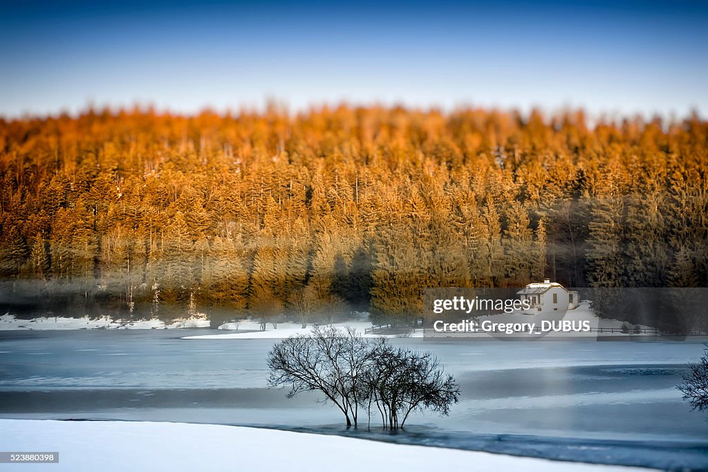 Frozen lake in winter with small remote cabin in forest