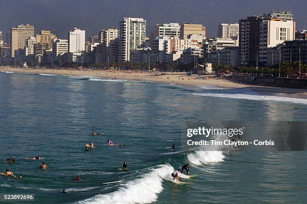 Early morning surfers at Ipanema beach catch a wave as the sunrise catches the light of the surrounding beachfront properties. Ipanema beach, Rio de...