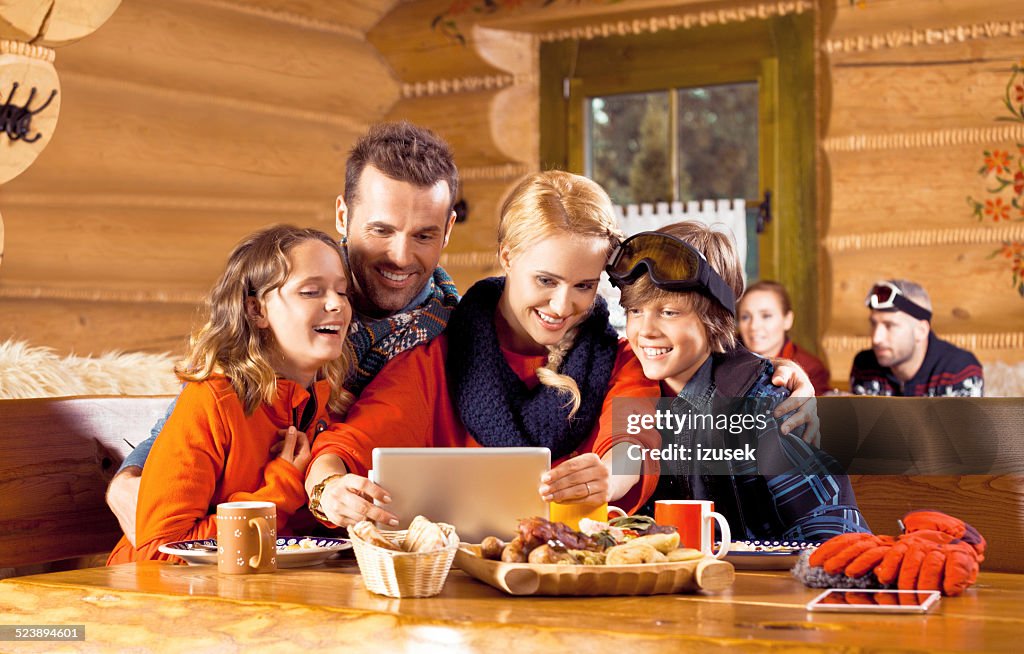 Family having lunch after skiing, using digital tablet