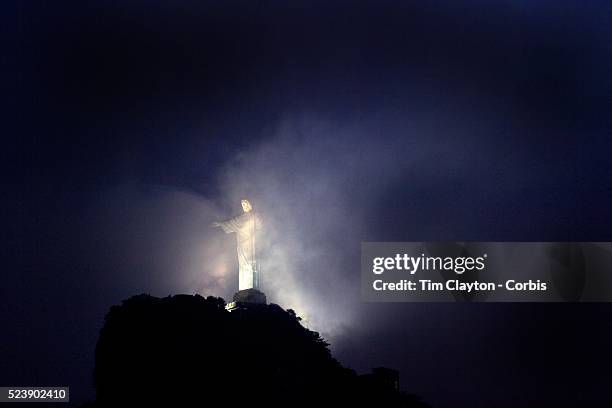 The iconic Cristo Redentor, Christ the Redeemer statue appears out of the clouds while lit up at night time atop the mountain Corcovado. The Christ...