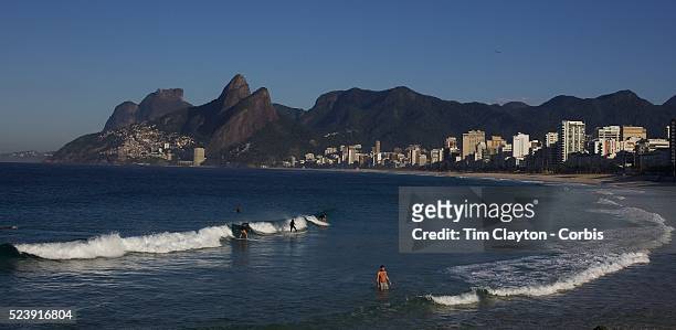 Early morning surfers at Ipanema beach catch a wave as the sunrise catches the light of the surrounding beachfront properties. Ipanema beach, Rio de...