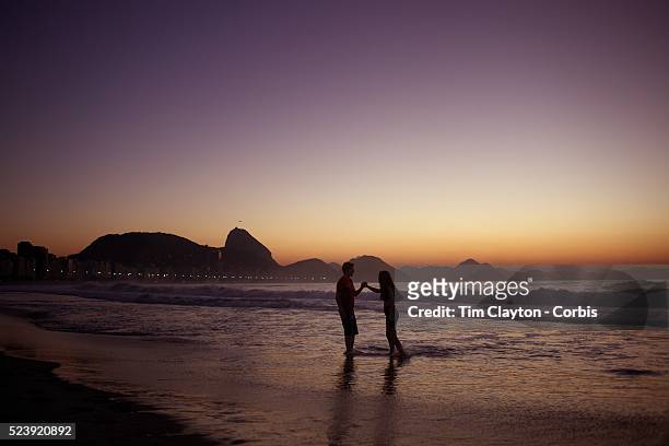 Couple enjoy a tender moment as they witness the amazing sunrise at Rio de Janeiro's most famous beach Copacabana with Sugar Loaf mountain in the...