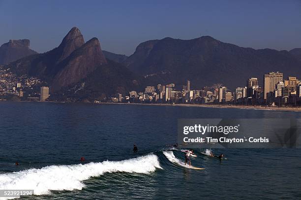 Early morning surfers at Ipanema beach catch a wave as the sunrise catches the light of the surrounding beachfront properties. Ipanema beach, Rio de...