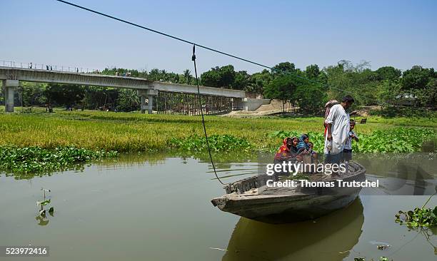 Narikelbari, Bangladesh Peoples cross a river by boat on April 10, 2016 in Narikelbari, Bangladesh. In the background a new bridge for the...