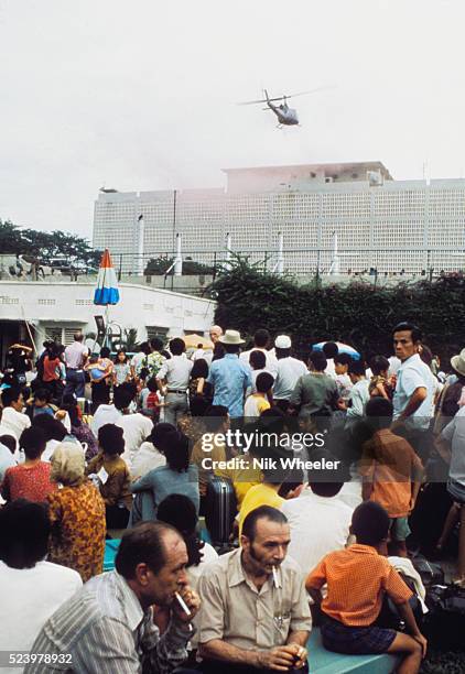Personnel and dependents and third country nationals huddle inside the American Embassy compound in Saigon as US Marine helicopter lifts small groups...