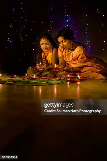 mother and daughter with diyas on diwali - rangoli stock-fotos und bilder