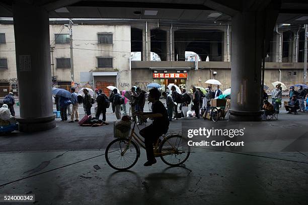 Man rides a bike past homeless people queueing to access a shelter in the slum area of Kamagasaki on April 23, 2016 in Osaka, Japan. Kamagasaki, a...