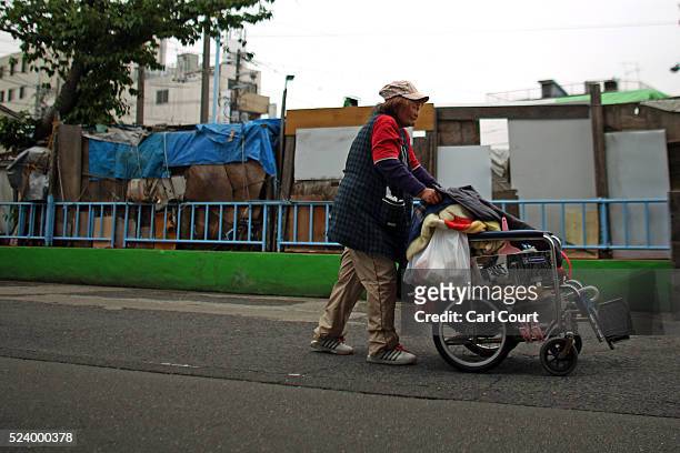 Homeless woman pushes a wheelchair past the slum area of Kamagasaki on April 24, 2016 in Osaka, Japan. Kamagasaki, a district in Japan's second...