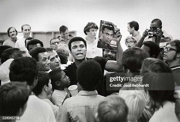 Muhammad Ali, surrounded by fans, emerges from a training session preparing for his fight with Jimmy Elllis yelling "I am the Greatest" and holding a...