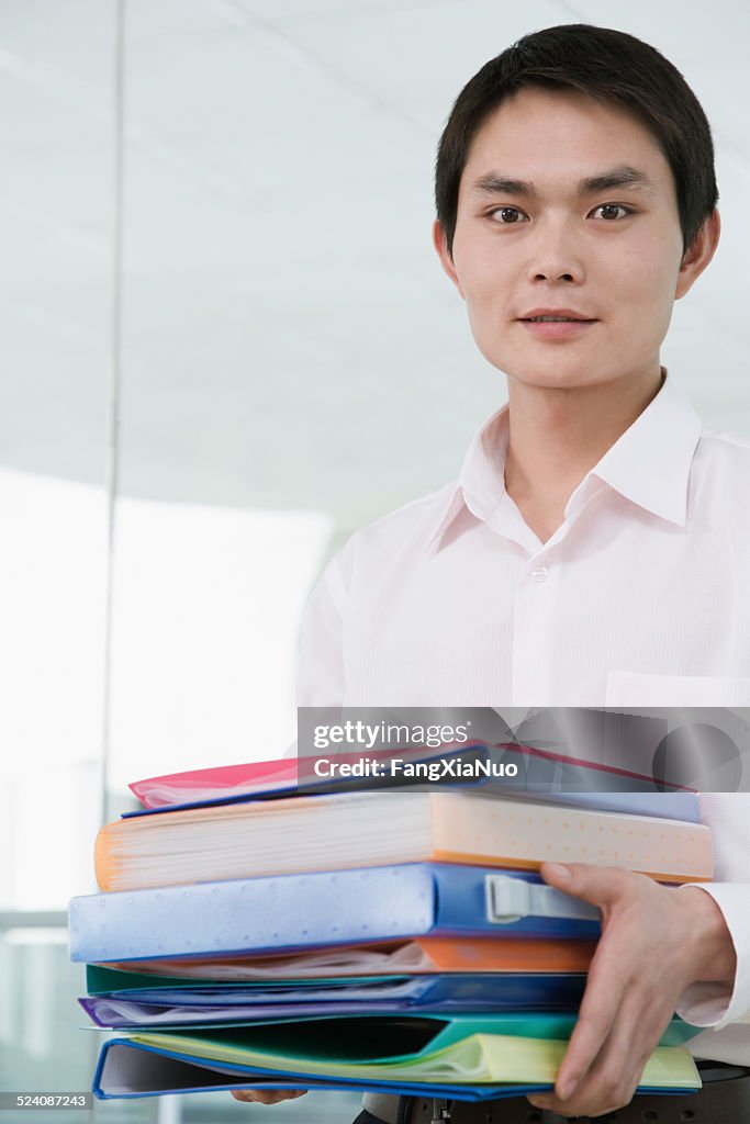 Homme d'affaires tenant une pile de fichiers, souriant, portrait