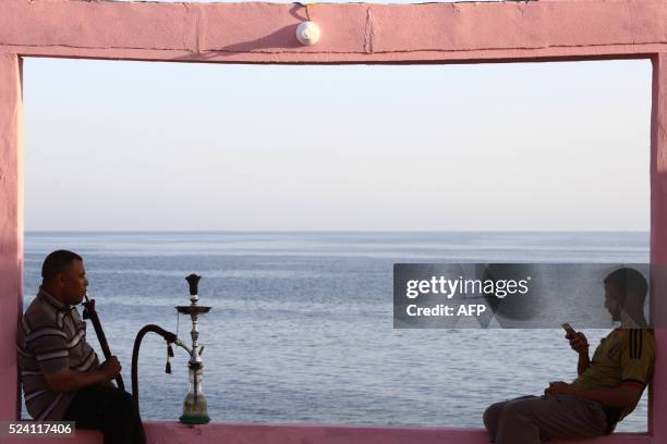 Two men sit on wall overlooking the Red Sea at a popular cafe in the northwestern Saudi town of al-Wajh on April 25, 2016. / AFP PHOTO / MOHAMMED...