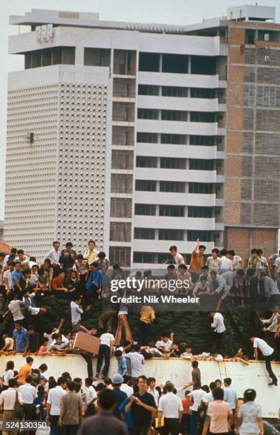 Desperate South Vietnamese clamber aboard barges in the port of Saigon in an attempt to escape from advancing North Vietnamese troops on the day of...