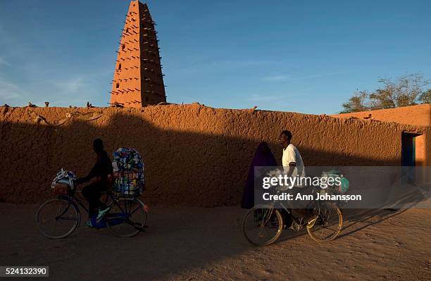 Salesmen ride their bicycles past the Grande Mosquee, the Grand Mosque, in Agadez, Niger. The mosque, which dates from 1515 but was rebuilt in 1844,...