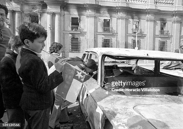 Child carrying a Chilean flag observes one of the cars that was parked in front of the presidential palace and was destroyed during the fighting....