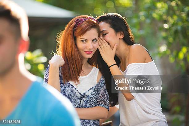 young woman whispering secret into friend's ear - woman whisper to man stockfoto's en -beelden