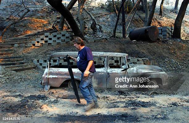 Paul Buchanan walks by a burnt out car in Palmer Canyon north of Claremont. NO SALES NEWSPAPERS IN NEW MEXICO | Location: Palmer Canyon, California,...