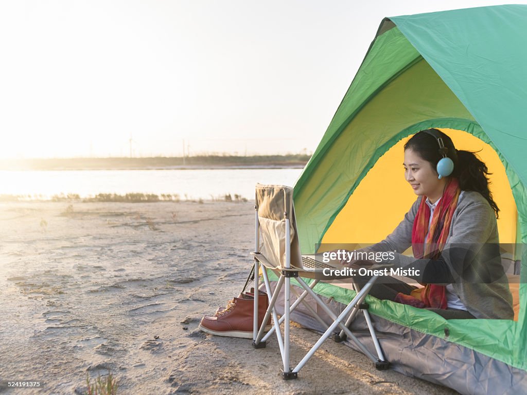 Young woman using laptop and sitting in tent.