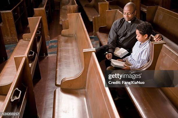 iglesia sacerdote y niño en banco de iglesia perteneciente a la lectura bible - reverendo clerecía fotografías e imágenes de stock