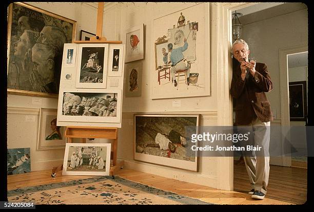 Norman Rockwell lights a pipe as he stands next to some of his paintings in the Norman Rockwell Museum at the "corner house" in Stockbridge,...