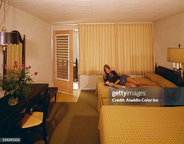 Young woman reads a magazine on a bed in her room at the "Castle in The Sand" motel.