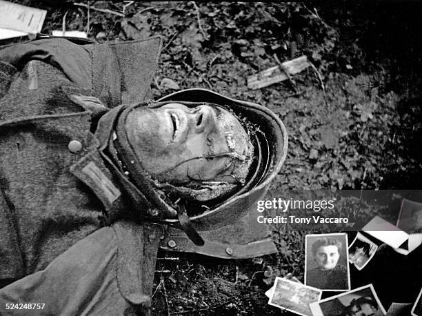 Dead German soldier killed during the Battle of the Bulge is seen surrounded by family photographs, Hürtgen Forest, Germany, World War II, December...