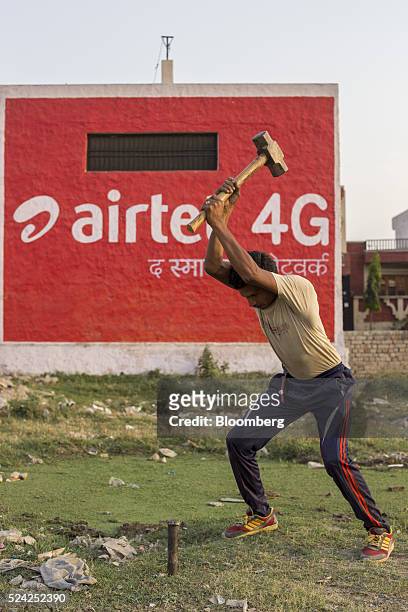 Worker uses a sledgehammer in front of a painted advertisement for Bharti Airtel Ltd. Displayed on the side of a building in Murthal, Haryana, India,...