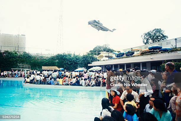 Evacuees inside the US Embassy surround the swimming pool as helicopter rescues stranded civilians trying to escape North Vietnamese troops about to...