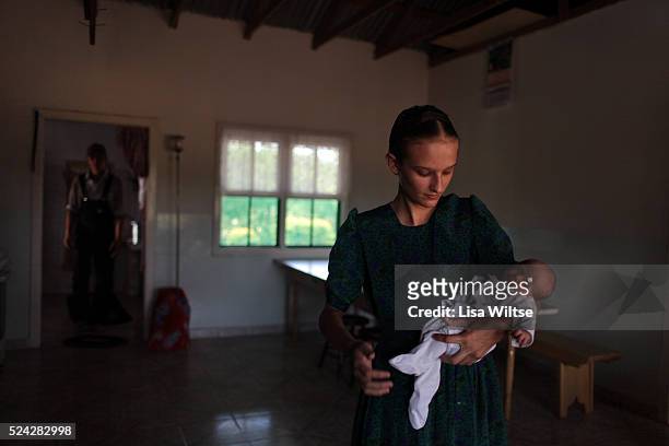 Manitoba, Bolivia. The Peter family. Mennonite teenager Maria holding a newborn baby in her home. Mennonite women are are not allowed to work outside...