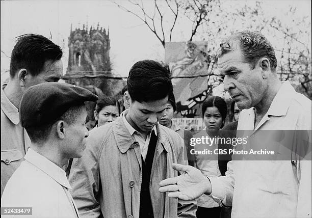 American broadcast journalist Charles Collingwood of CBS News talks to several Vietnamese civilians near a bomb damaged church and a propaganda...