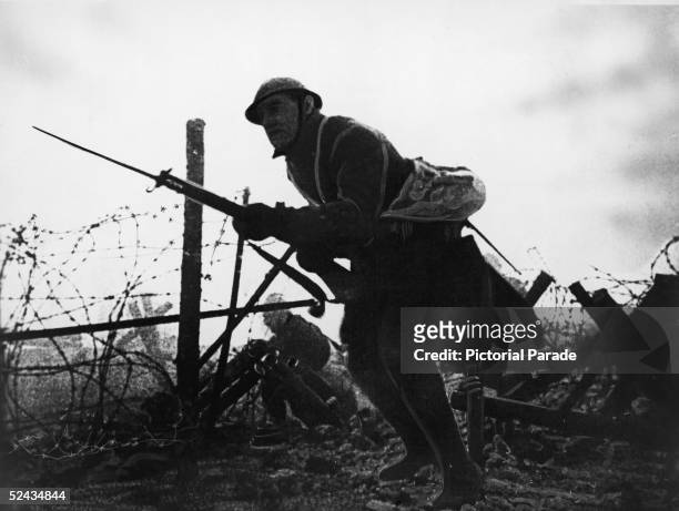 Retouched photograph of an Allied soldier as he stands with fixed bayonet across No Man's Land amid barbed wire obstacles during a battle on the...