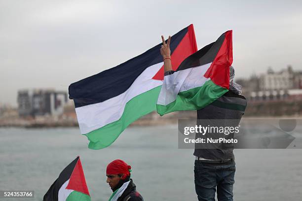 A Palestinian young holds national flags as he makes a victory sign during a protest against the blockade on Gaza, at the seaport of Gaza City...