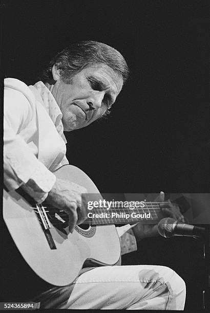 Country musician Chet Atkins sits on stage, playing his acoustic guitar.