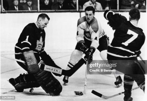 Jean Beliveau of the Montreal Canadiens flicks the puck between the legs of goalie Johnny Bower of the Toronto Maple Leafs while Bower's teammate Tim...