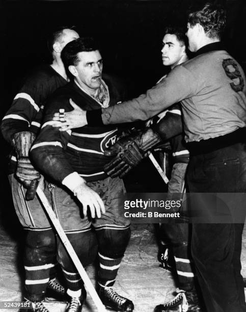 Maurice 'Rocket' Richard of the Montreal Canadiens is restrained by linesman George Hayes after Richard was boarded by Bob Bailey of the Toronto...