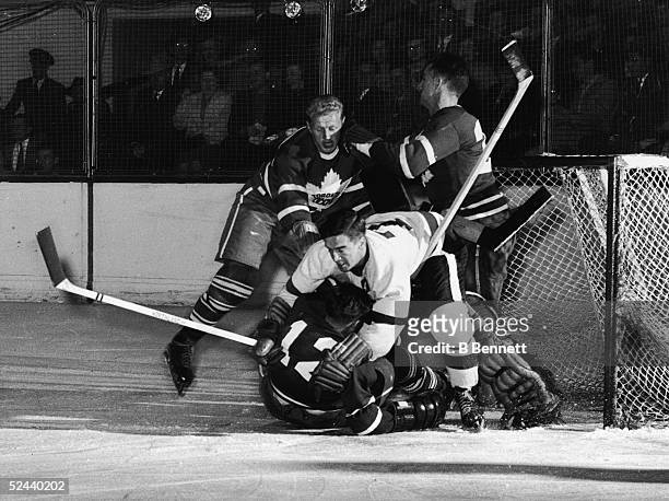 Ted Lindsay of the Detroit Red Wings collides with Fern Flaman of the Toronto Maple Leafs, while Leafs goalkeeper Al Rollins tries to keep an eye on...