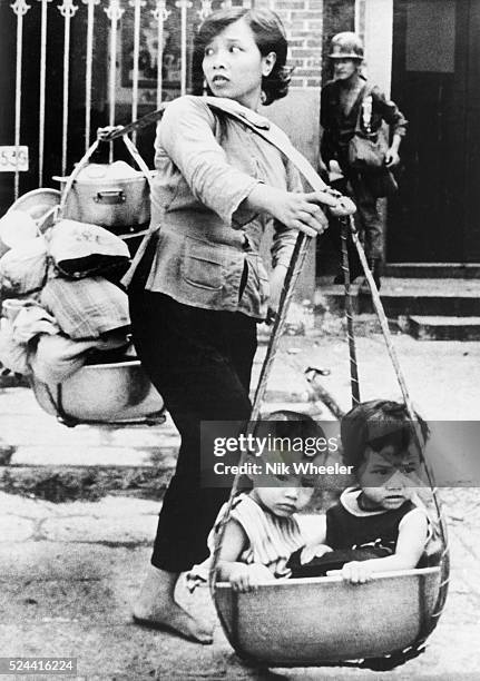 Vietnamese woman carries her children and possessions on bamboo pole as she tries to escape fierce fighting in the Cholon suburb of Saigon during the...