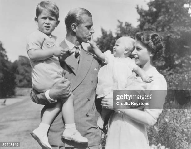 Prince Charles aged two, in the arms of his father, the Duke of Edinburgh. His mother, the then Princess Elizabeth, holds Princess Anne, as they walk...