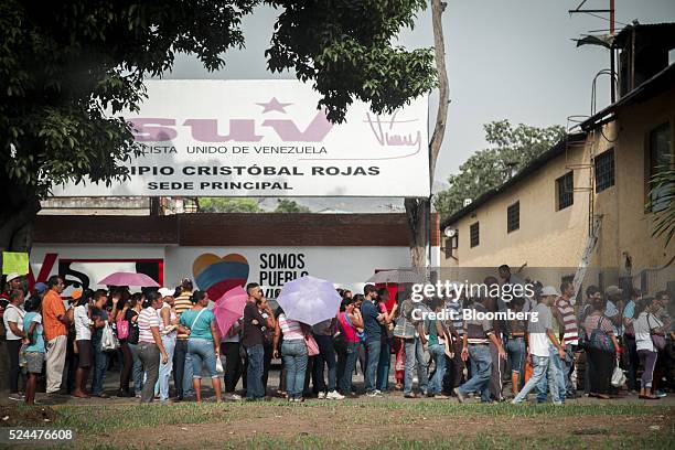 People stand in front of a Socialist Party office while waiting in line to buy groceries at a supermarket in Charallave, Venezuela, on Monday, April...