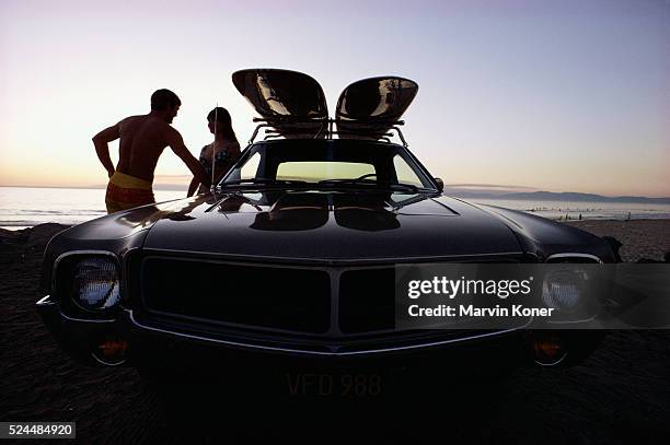 Surfers and their surfboards in silhouette as they stand beside an AMC Javelin with the boards mounted on the roof rack, circa 1970.