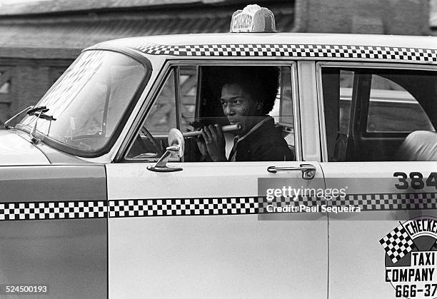 Cabdriver plays the flute while driving in the city streets, Chicago, Illinois, 1980s.