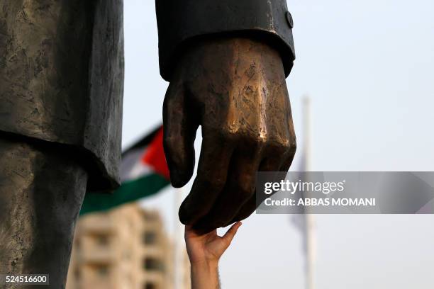 Palestinian man touches the hand of a giant statue of Nelson Mandela following its inauguration ceremony in the West Bank city of Ramallah on April...