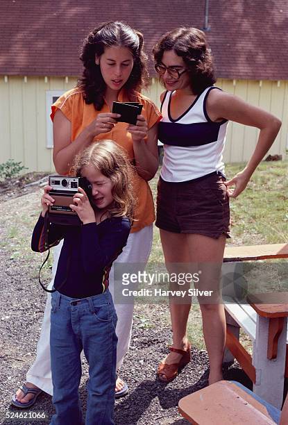 Women look at photographs while a girl takes pictures with a Kodak instant camera, 1979.