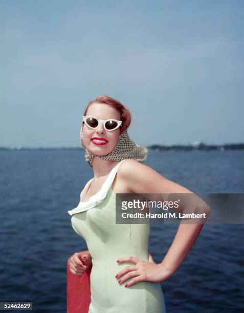 Woman in a swimsuit by the ocean looks at the camera and smiles with her hand on her hip, 1956.