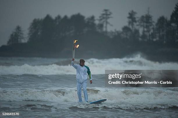 Surfer Raphael Bruhwiler rides a surfboard with the Olympic flame during the Olympic torch relay on Long Beach in Pacific Rim National Park near the...