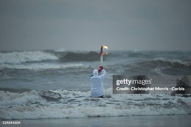 Ruth Sadler carries the Olympic flame into the surf during the Olympic torch relay on Long Beach in Pacific Rim National Park near the town of...