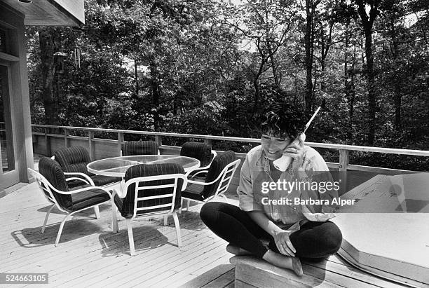 Woman using a telephone on an outside decked area of a house, East Hampton, New York, USA, May 1992.