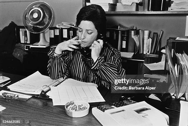 Bookkeeper smoking a cigarette at her desk while she works, New York City, USA, 15th December 1982.